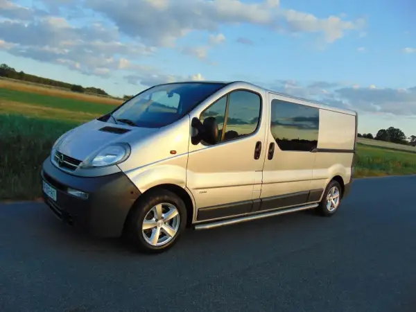 Srebrny Opel Vivaro 2.5 CDTI na drodze, zachód słońca. Wiele osób szuka opinii na forum o tym modelu.