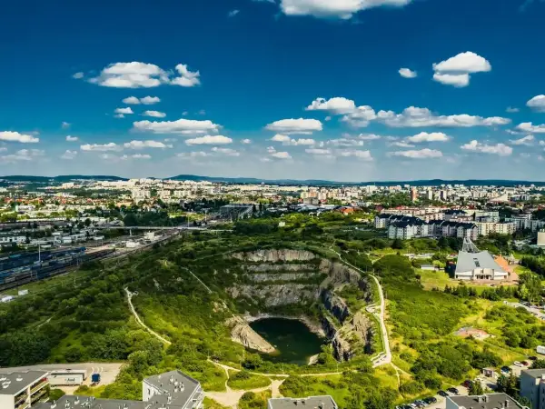 Rezerwat skalny Ślichowice z jeziorem w wyrobisku, otoczony zielenią i zabudową miejską pod błękitnym niebem.