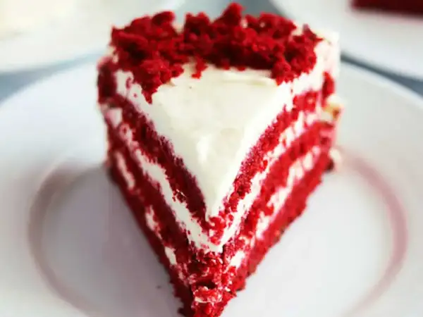 En saftig bit red velvet cake med krämig frosting och smulor på toppen.