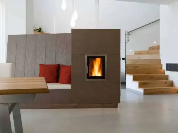 Moderner Wohnraum mit gemütlicher Sitzbank, Kamin und Holztreppe. Die Pelletheizung im Kamin sorgt für Wärme, die Vorschriften sind eingehalten.