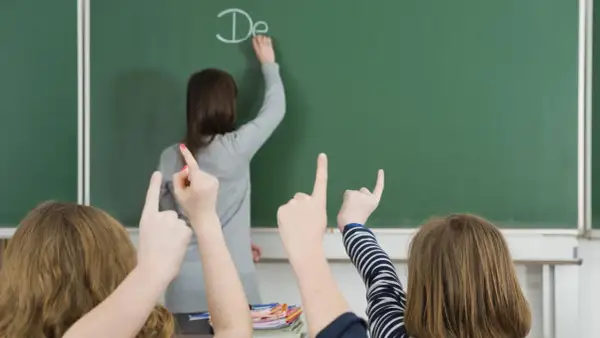 Lehrerin schreibt "De" an Tafel, Schüler heben Hände. Einblick in die bildungspolitik deutschland.