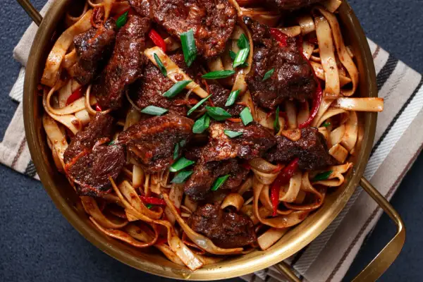 Aksamitne kawałki wołowiny po seczuańsku z makaronem ryżowym, papryczkami chili i szczypiorkiem w złotej misie.