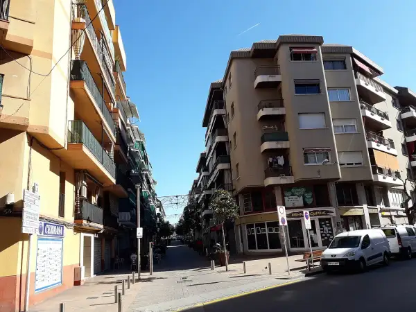 Calle soleada en Les Roquetes del Garraf, con edificios residenciales y comercios.