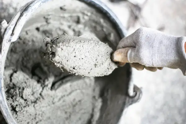 Mano guantata raccoglie cemento fresco da un secchio. I materiali leganti sono pronti per l'uso.