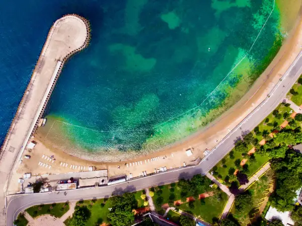 Vista aerea di una spiaggia e di un molo a Istanbul, dove c'è il mare turchese e una strada costiera con un parco verde.