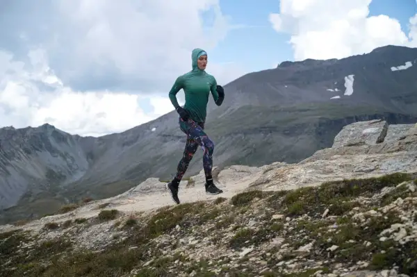 Kobieta w sportowym stroju biegnie po górskim szlaku, utrzymując rytmiczną kadencję bieganie.