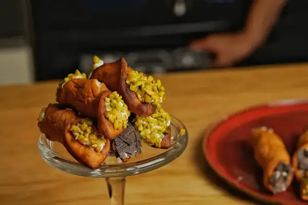 Ein Glasständer voller Cannoli, bestreut mit Pistazien und Schokolade. Ein köstliches Cannoli-Rezept zum Nachmachen.