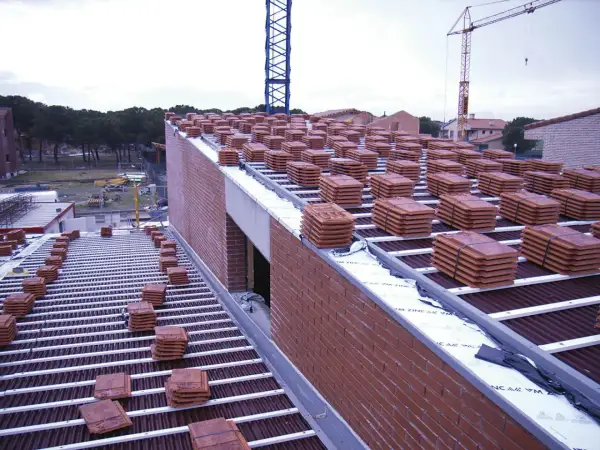 Pilotes de tejas rojas apiladas en la cubierta de una casa en construcción. Grúas en el fondo.