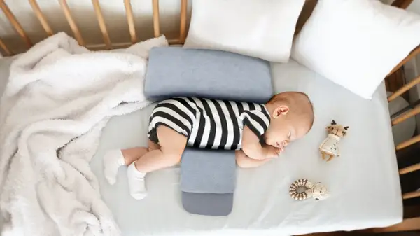 Noworodek śpi na boku, podtrzymywany przez poduszkę klin. Czy poduszka klin jest bezpieczna dla noworodka? Tak, jeśli jest używana zgodnie z zaleceniami.