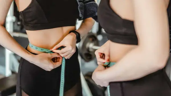 Donna in palestra misura la vita con un metro, segno di un percorso di dimagrimento.