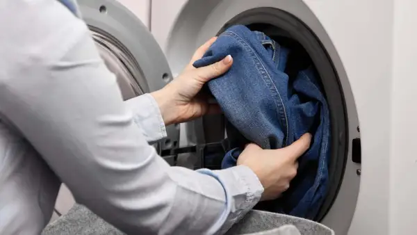 Hände legen Jeans in die Waschmaschine. Das passende Jeans waschen Programm wird ausgewählt.