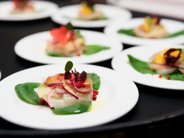 Carpaccio de saint jacques frais, garni de pamplemousse, oignons rouges et pousses sur des feuilles d'épinards.