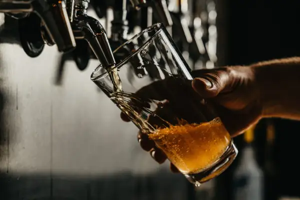 Un bicchiere viene riempito con una birra dorata e spumeggiante, probabilmente una birra 14 gradi, da un rubinetto di metallo.