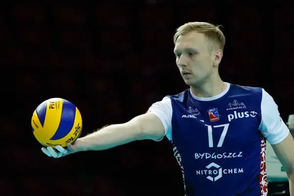 Siatkarz Mateusz Sacharewicz z piłką w dłoni, gotowy do zagrywki.