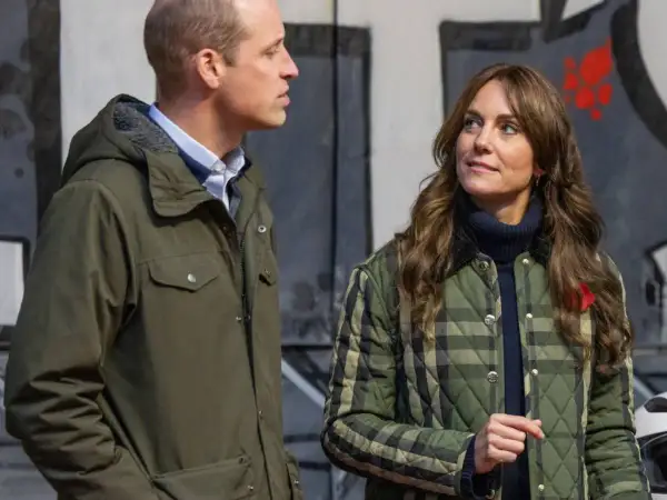 William van Wales y Kate Middleton, ambos con chaquetas, conversan frente a un mural.