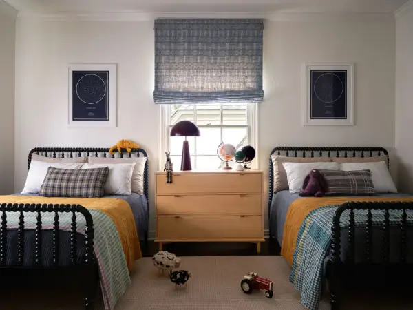 Twin beds with colorful quilts and star charts create fun boys bedroom ideas. A wooden dresser holds globes and a lamp.