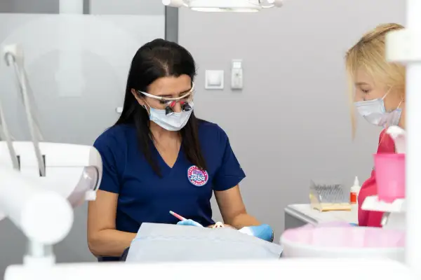 Dentystka w okularach powiększających i masce pracuje nad pacjentem, który odczuwa drętwienie po znieczuleniu zęba.