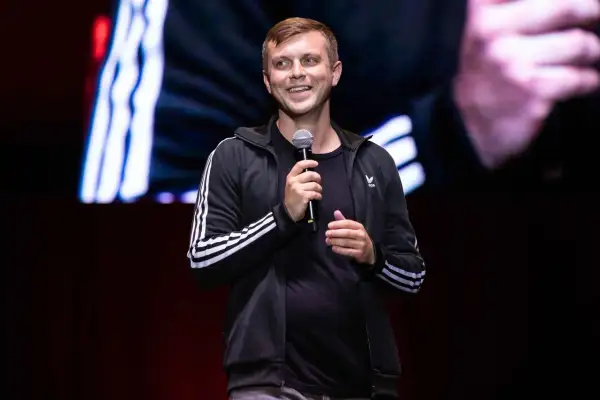Uśmiechnięty Krajewski na scenie, trzyma mikrofon. Jego stand up rozgrzewa publiczność.