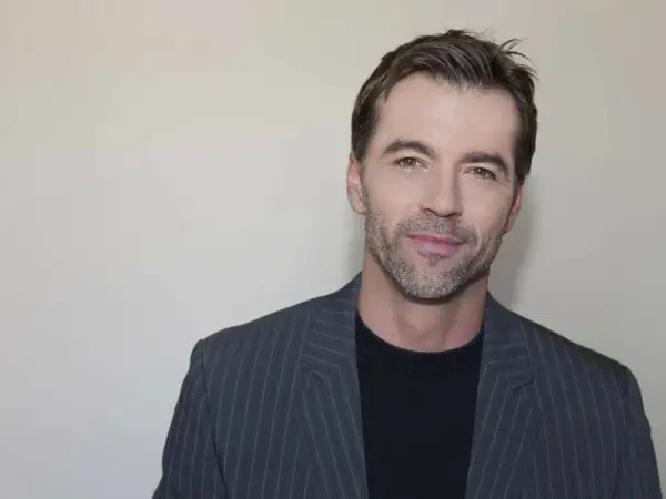 Un homme d'environ 40 ans, le regard franc, porte une veste à fines rayures grises sur un pull noir.