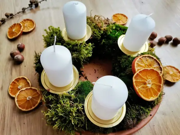 Corona dell'avvento fai da te con muschio, candele bianche, fette d'arancia essiccata e nocciole.