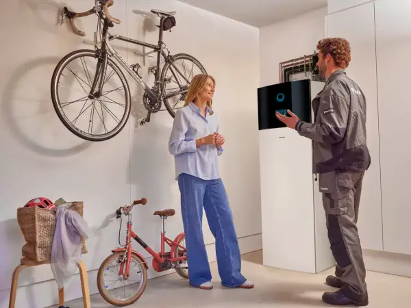 Técnico explica a una mujer el **rendimiento estacional aerotermia** junto a una unidad Daikin. Bicicletas colgadas al fondo.