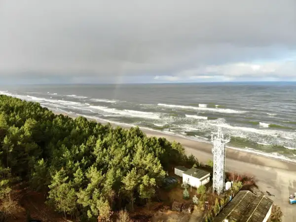 Plaża Kąty Rybackie z wieżą widokową i lasem sosnowym. Na niebie tęcza.