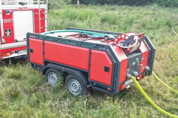 Nowa zabudowa pożarnicza na przyczepie, gotowa do akcji. Wąż strażacki zwinięty na bębnie, czekający na sygnał.