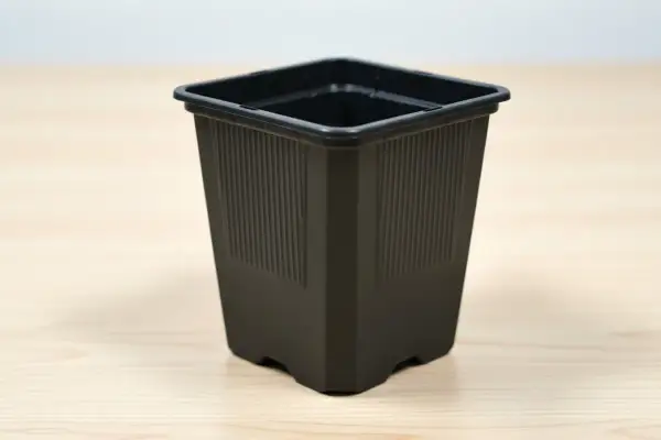 En svart, fyrkantig kruka med räfflade sidor står på ett ljust träbord. Perfekt för dina små plantor.