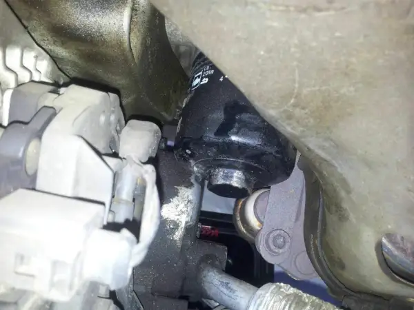 Schwarzer Ölfilter an einem Auto-Motor, umgeben von Metallteilen und Kabeln.