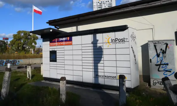 Paczkomat InPost z logo Allegro Smart. W tle polska flaga i budynek. Ile jest paczkomatów w Polsce? Tysiące!
