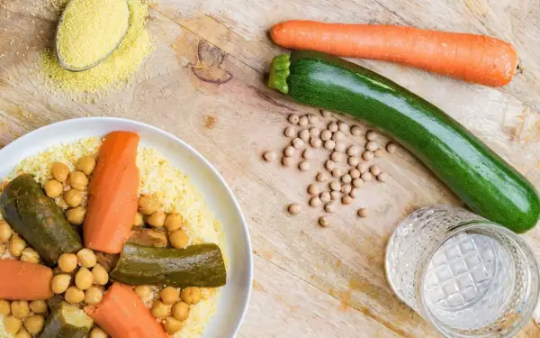Un plat de couscous aux légumes, pois chiches, carottes et courgettes. Une cuillère de semoule est à côté.