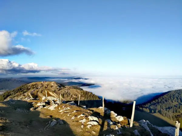Vue panoramique d'une randonnée la Dôle depuis les Dappes, avec une mer de nuages sous un ciel bleu éclatant.