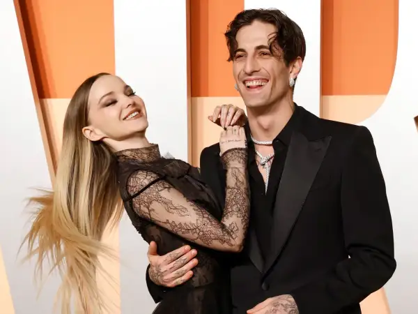 La pareja Dove Cameron y Dylan Sprouse ríen juntos, ella con un vestido de encaje negro y él con un traje negro.