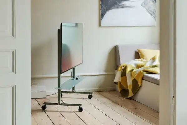 Moderner fernseher im schlafzimmer auf einem grünen Rollwagen, daneben eine gemütliche Bank mit karierter Decke.