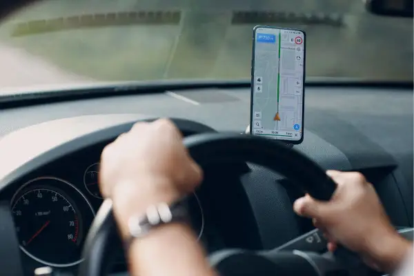 Ręce na kierownicy, smartfon z nawigacją na Androida pokazuje trasę.