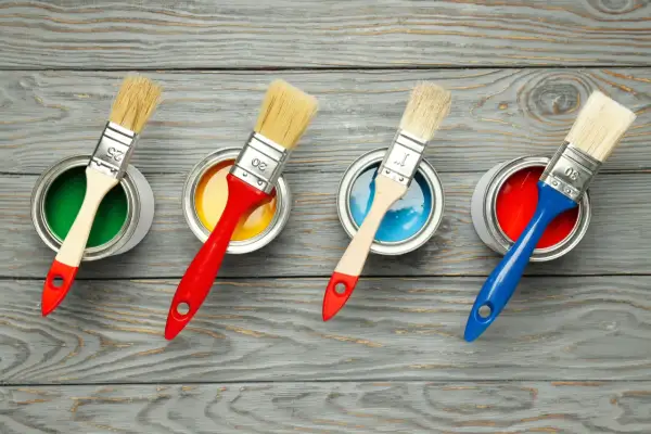 Quattro barattoli di vernice colorata (verde, giallo, blu, rosso) con pennelli pronti all'uso. La scelta della vernice giusta per il legno è fondamentale per un buon risultato.