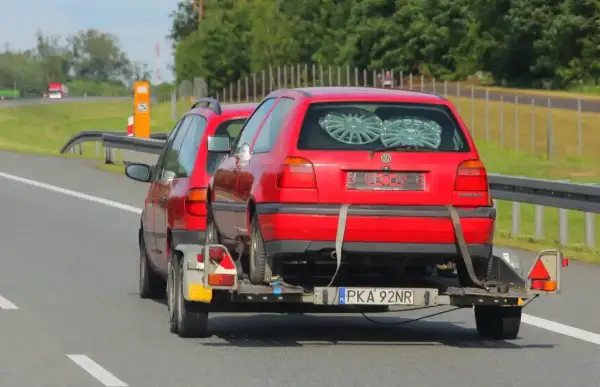 Czerwony Volkswagen Golf na lawecie, holowany przez inny samochód. To dowód, że automatem można holować inne auto, choć nie jest to standardowa sytuacja.