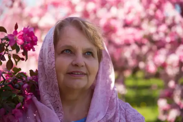 Uśmiechnięta Zuzanna w różowym szalu, otoczona kwitnącymi drzewami. Piękny dzień na imieniny Zuzanny.