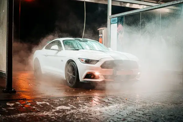 Biały Mustang w obłokach pary podczas mycia aut. Woda spływa po karoserii, tworząc efektowną mgiełkę.