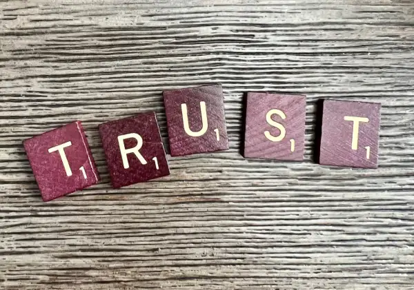 Litery "TRUST" ułożone na drewnianym tle. Brak zaufania w związku czy to ma sens?