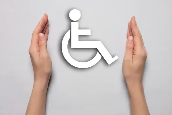 Dwie dłonie otaczają symbol osoby na wózku inwalidzkim, symbolizując wsparcie dla osób, na jakie choroby można dostać orzeczenie o niepełnosprawności.