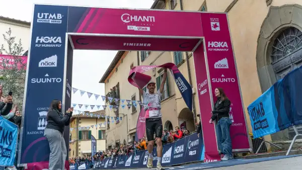 Un coureur franchit la ligne d'arrivée du Chianti by UTMB, acclamé par la foule. Il tient une banderole rose de finisher.