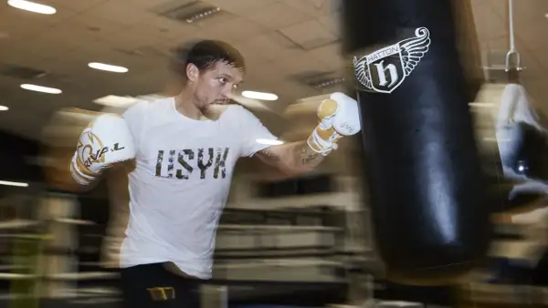 A boxer in a white t-shirt and gloves trains intensely during a boxing training camp, punching a heavy bag.