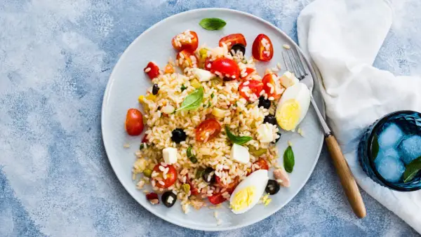 Un piatto colorato di insalata di riso con pomodorini, olive, mozzarella e uova sode. Perfetta per un pasto estivo.