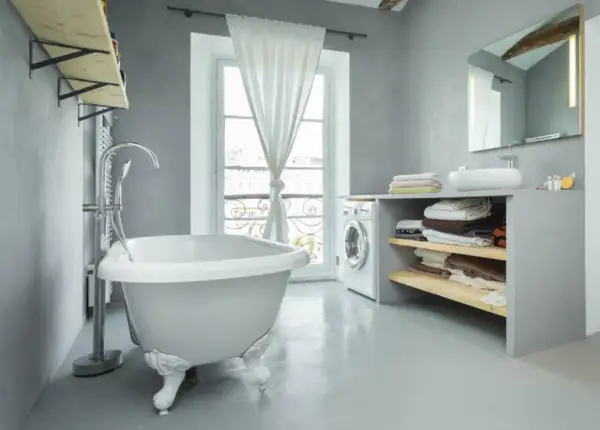 Un baño moderno con bañera independiente, lavadora y estantes con toallas. La idea de pintar bañera aquí es para un estilo minimalista.