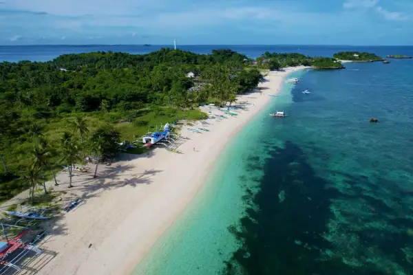 En vit sandstrand med palmer och traditionella filippinska båtar. Vattnet är turkost och klart, med en grönskande ö i bakgrunden. En idyllisk vy från Cebu, Filippinerna.