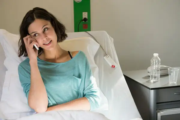 Kobieta w szpitalnym łóżku rozmawia przez telefon, szukając informacji, co niszczy raka.