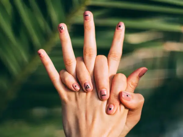 Manos con uñas flamencas en tono rosa pálido, decoradas con pequeños triángulos y puntos negros.