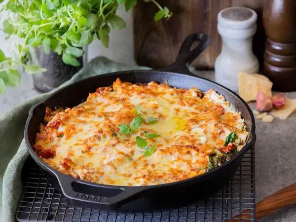 En gyllene, bubblande vegetarisk lasagne i gjutjärnspanna, toppad med färska örter. Perfekt för en mysig middag.