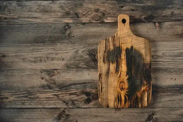Planche à découper en bois brut, brûlée et texturée, sur un fond de planches de bois vieilles. Idéal pour apprendre comment traiter une planche de bois brut.